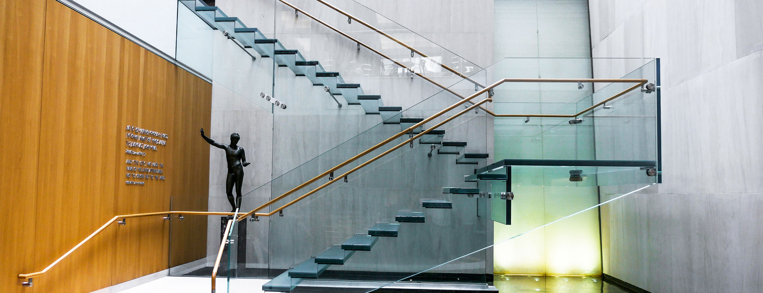 Side view of the all-glass staircase at the Onassis Cultural Center showcasing the stairs, ballustrades and railing.